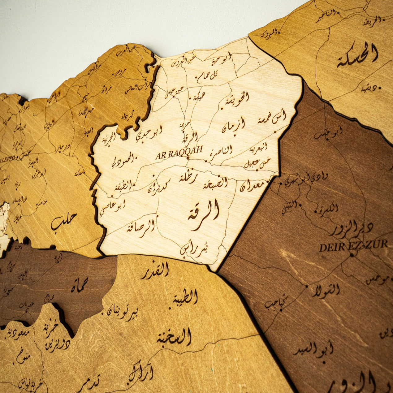 Wooden map of Syria with Arabic text on a light gray background
