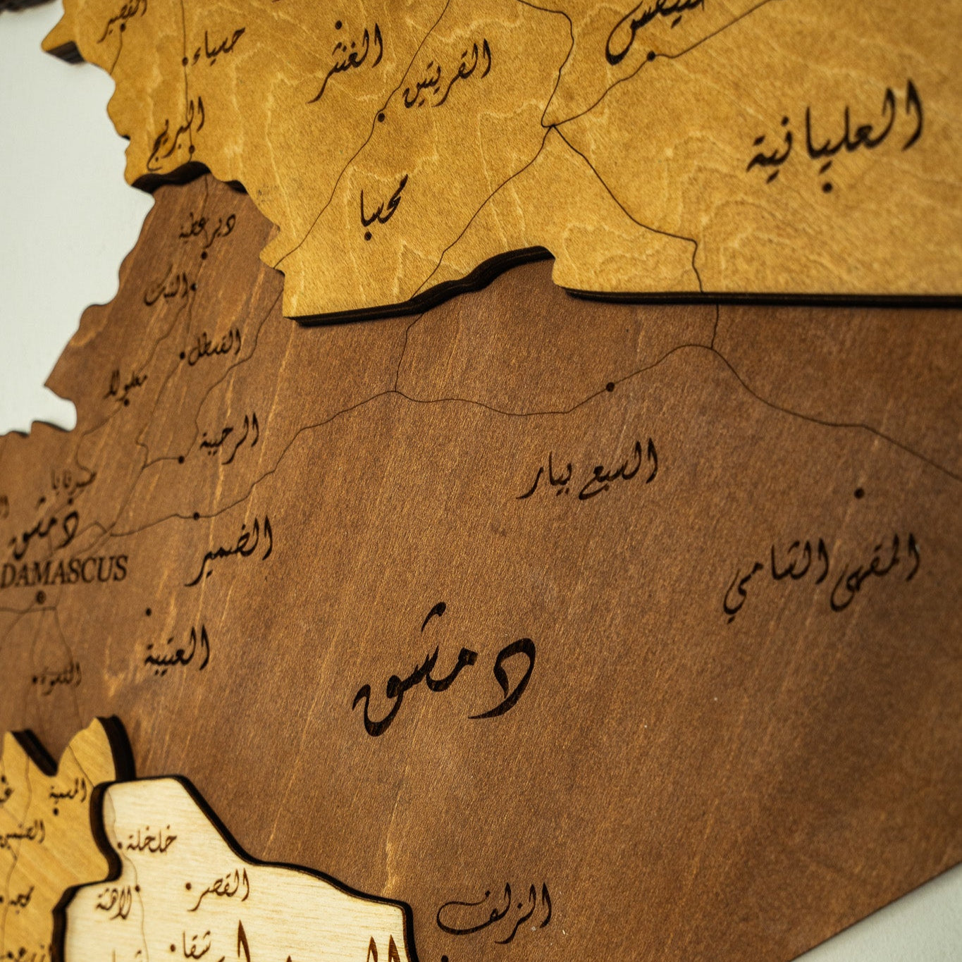 Wooden map of Syria with Arabic text on a light gray background