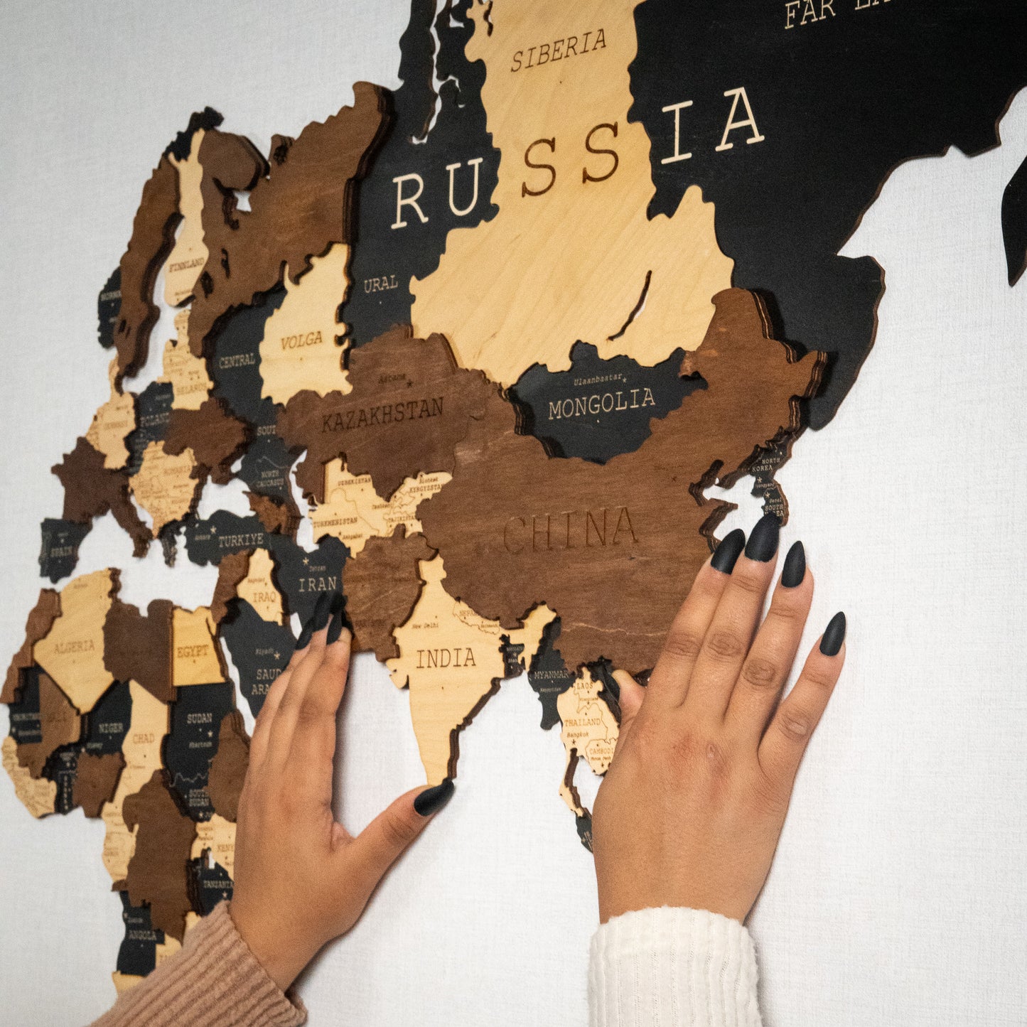 Wooden world map with hands holding it against a light background