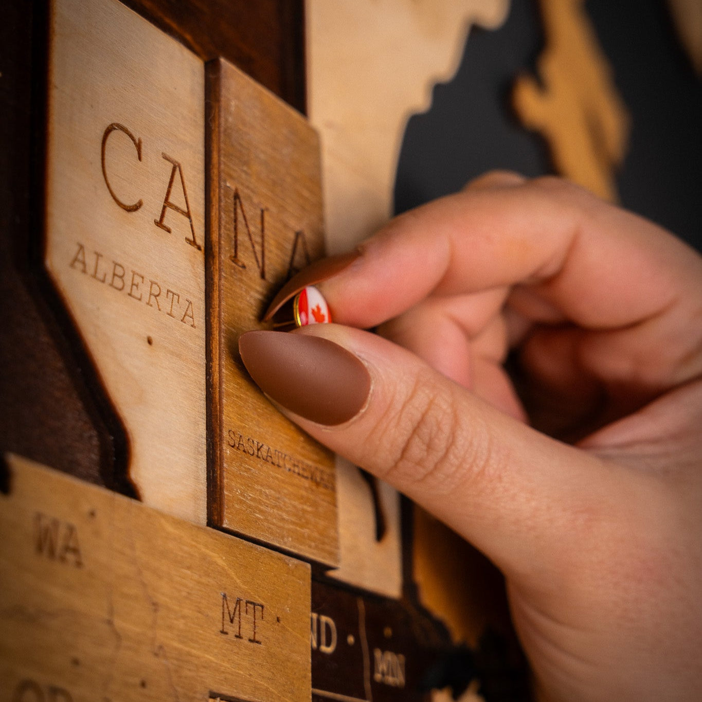 Person pinning country Canada using push pins on wooden world map