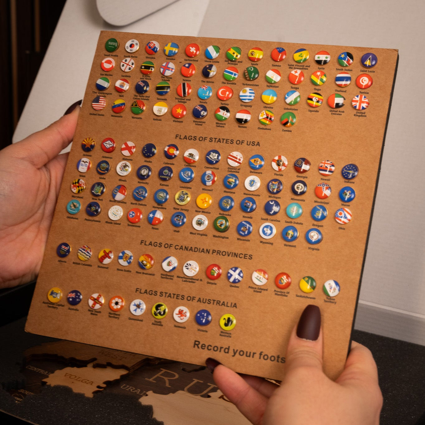 Cardboard with push pins of various countries held by two hands.