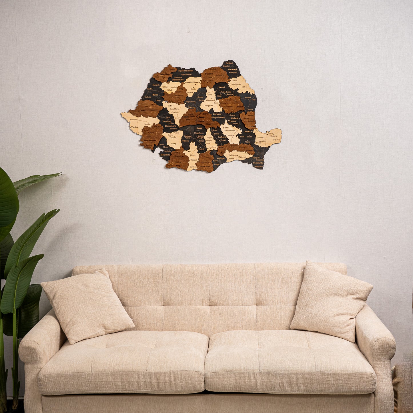 Wooden wall art of Romania map on a light gray wall above a beige sofa.