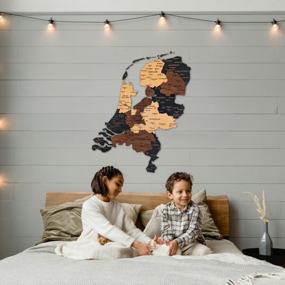 Two children sitting on a bed with a wooden wall art map of netherlands above them.