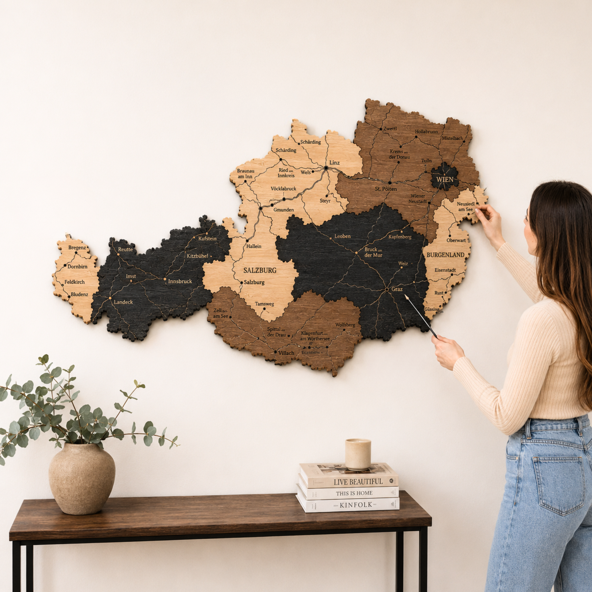 Woman interacting with a wooden map of Austria on a wall, with a table and plant in the foreground.