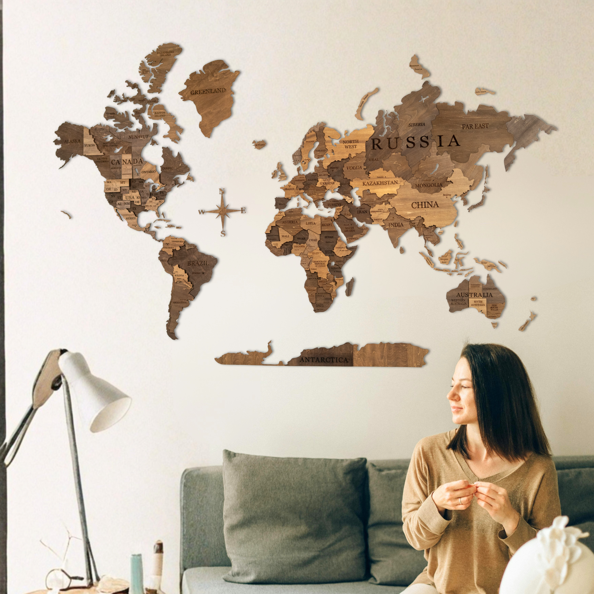 Woman sitting on a couch in a living room with a wooden world map on the wall.